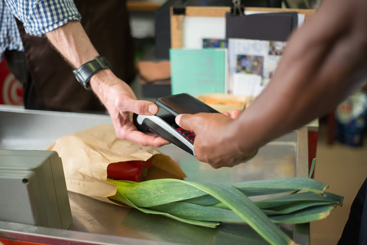services-01 A customer making a contactless payment with a smartphone at a grocery store checkout counter.