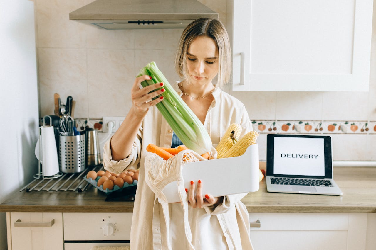 why-choose-us Woman unpacks fresh vegetables from delivery box in a modern kitchen setup with a laptop nearby.